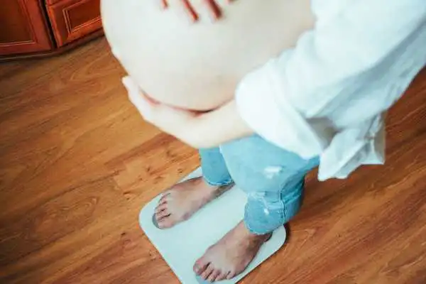 Image of woman weighing herself and experiencing weight gain through pregnancy Bury St Edmunds